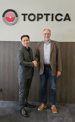 Lawrence Chua, Managing Director of AceXon Technologies (left), and Thomas Renner, President (CSO) of TOPTICA Photonics AG (right), shake hands in front of the TOPTICA Photonics AG logo.